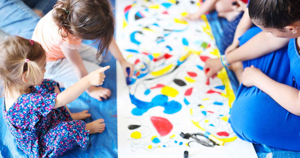 Plusieurs enfants et une adulte en train de colorier une fresque posée par terre