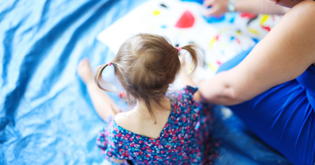 Enfant assis de dos regardant un dessin posé par terre