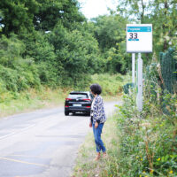Une femme attendant devant un arrêt de bus. Au loin, une voiture