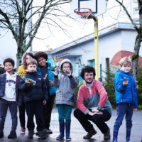 Un groupe d'enfants tenant des Lego dans les mains, avec un animateur périscolaire, sur un terrain de basket dans le secteur des écoles dans le quartier Château.