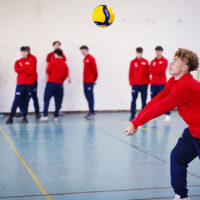 Jeune en train de jouer au volley avec le reste de l'équipe derrière.